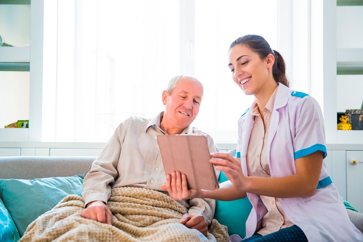 vantaggi assistenza a domicilio per anziani non autosufficienti. Nella foto assistente domiciliare tiene compagnia ad anziano malato